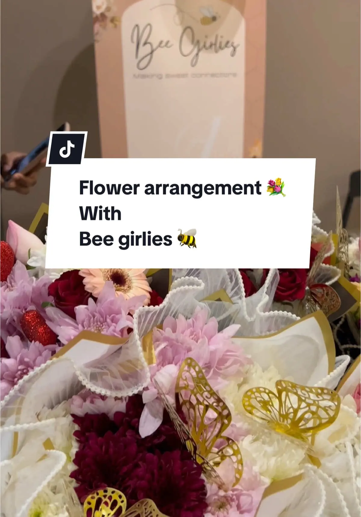Wrapped bouquets of pink and burgundy chrysanthemums and gerberas with gold butterfly details at a floral arrangement workshop.
