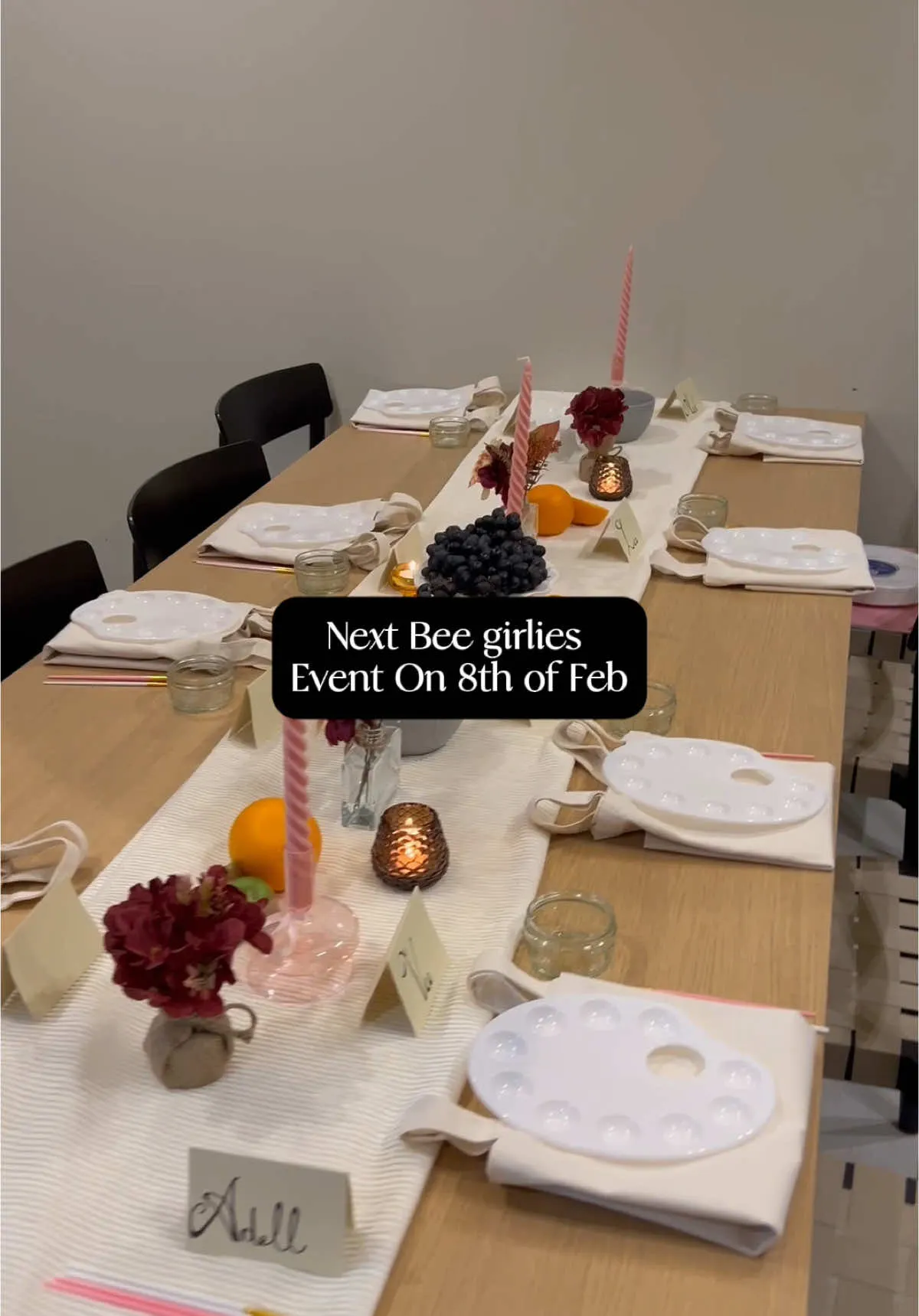 A long table set for a creative workshop with paint palettes, linen napkins, taper candles, fruit and small floral arrangements.